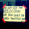 a photo of a taped-up sign reading: DO NOT USE THE REFLECTION OFF THIS GLASS TO CHECK YOURSELF OUT